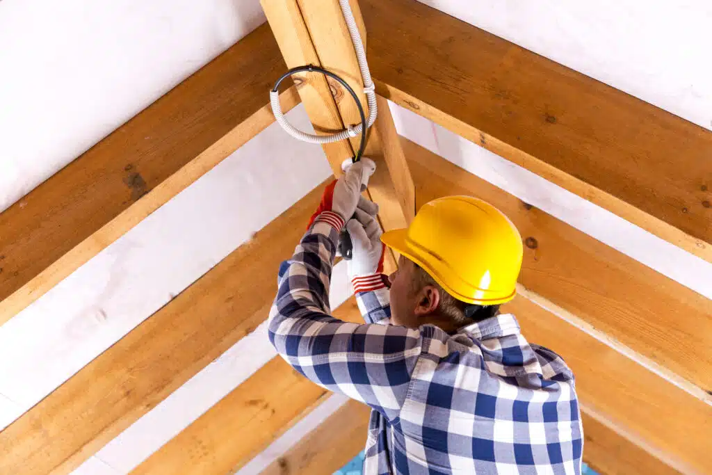 Electrician working with wires at attic renovation site, Electrical Insulation.